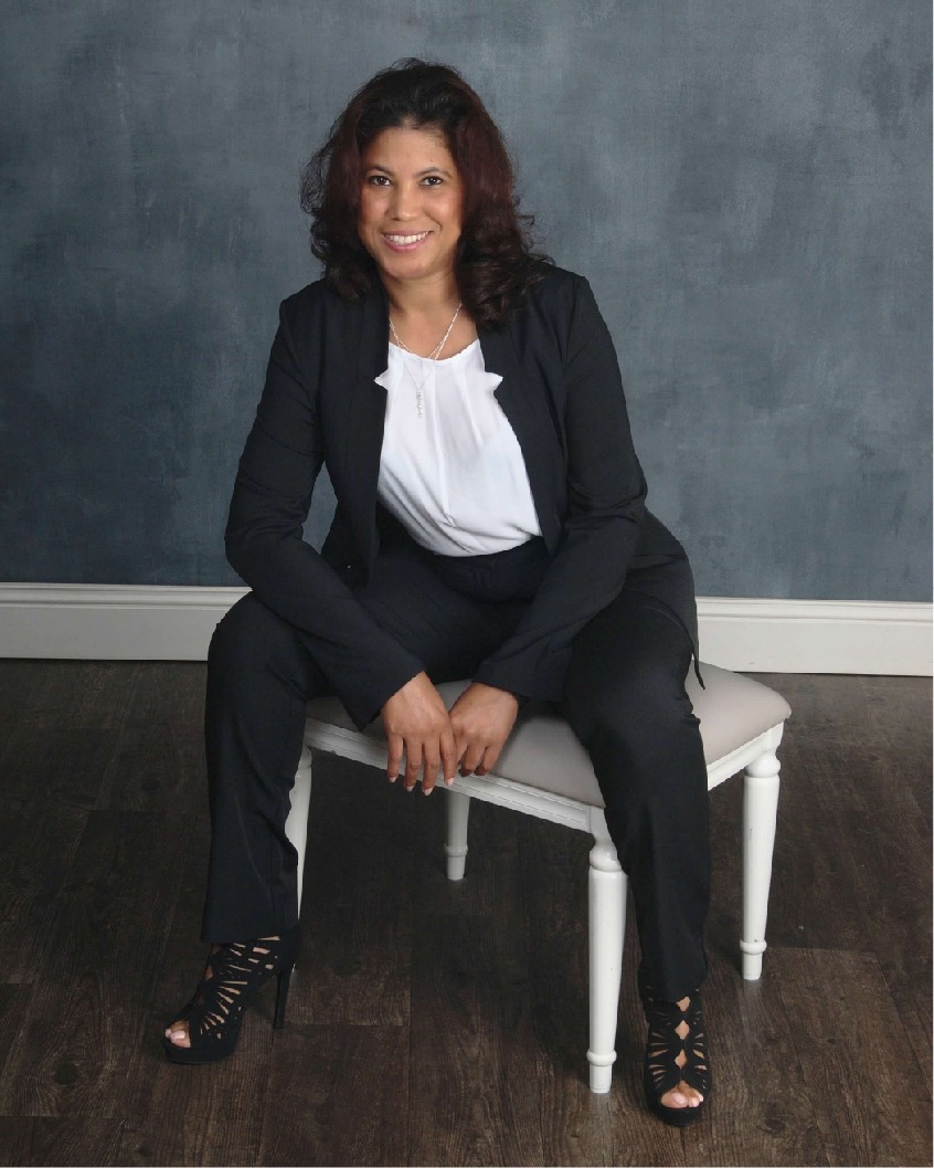 Ysaura Inoa seated on a white bench in a black suit